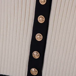 Macro detail of cream ribbed knit dress featuring gold crest buttons and black contrast trim