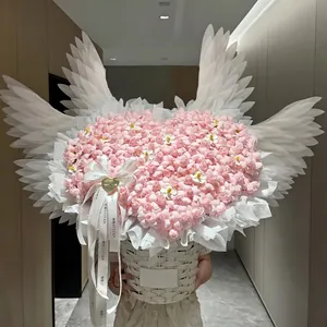 Grande composizione di fiori rosa a cuore con ali di piume elettriche in un cesto bianco.