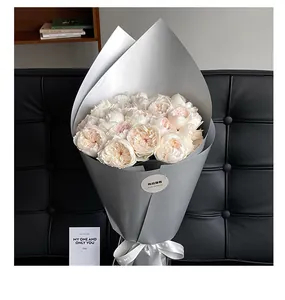Detail of matte silver pearlized paper wrapping a rose bouquet on a black leather sofa