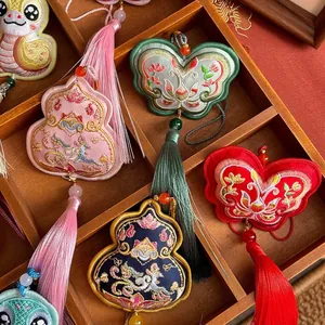 Traditional Chinese embroidered sachet pendants with butterfly and gourd designs in a wooden tray.
