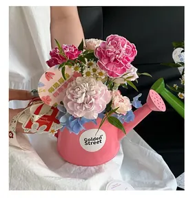 Gros plan d'un arrangement floral en arrosoir rose avec des œillets et des étiquettes.