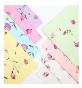 Primer plano de papel artesanal de colores con pétalos de flores y hojas naturales reales.