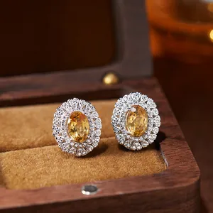 Detailed macro shot of oval yellow gemstone stud earrings in a wooden jewelry box.