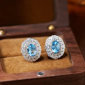 Close-up of elegant blue topaz stud earrings with halo diamonds in a wooden jewelry box