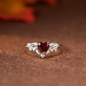 Détail macro de bague grenat en cœur avec accents de feuilles d'argent et zircons