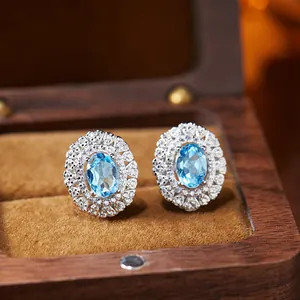 Detailed macro view of elegant oval blue topaz earrings with CZ halo in a wooden gift box.
