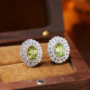 Detailed macro shot of oval green gemstone earrings with double halo in a wooden box