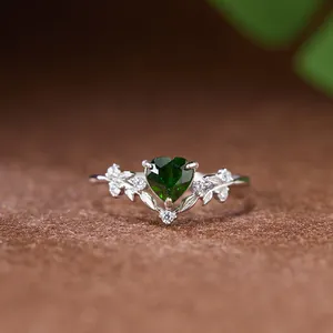 Gros plan d'une bague en argent s925 avec motif feuilles et gemme cœur verte