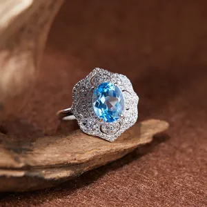 Gros plan d'une bague topaze bleue ovale avec une monture en argent style dentelle