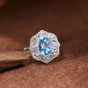 Gros plan d'une bague en argent S925 avec topaze bleue et un halo en dentelle délicat.