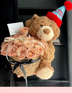 Chestnut plush teddy bear with birthday hat holding a peach rose bouquet in a straw basket