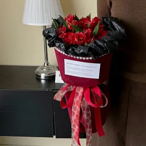 Red flower bouquet wrapped in burgundy paper with rose patterned ribbon for gifting