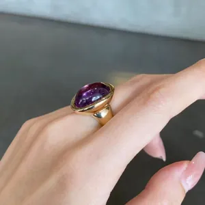 Close-up of a luxury purple amethyst bathtub ring in gold finish on a finger.