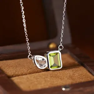 Close-up of a silver necklace with emerald-cut green and teardrop white gems.