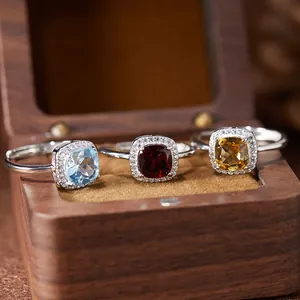 Detail view of S925 silver rings set with colorful square gemstones in a wooden box