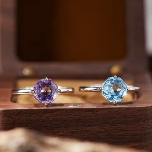 Close-up of octagonal amethyst and blue topaz rings in a wooden jewelry box