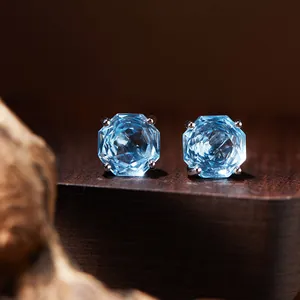 Macro view of light blue octagon-cut topaz stud earrings on dark wood display stand