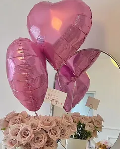 Close-up of pink heart-shaped foil balloons with soft pink roses background