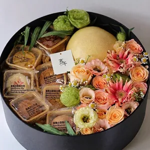 Large round black gift box filled with fresh flowers, mooncakes, and a pomelo