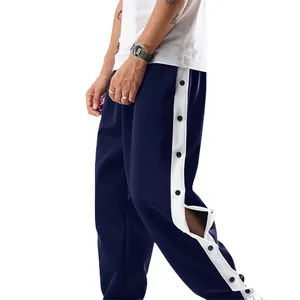 Detail van een donkerblauwe sportbroek met witte zijstrepen en handige drukknopen aan de zijkant.