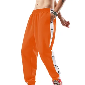 Detail van de oranje heren sportbroek met witte zijstrepen en zwarte drukknopen op de zijkant.