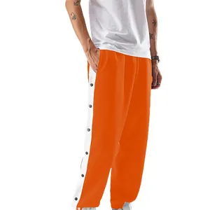 Detail van oranje heren sportjoggingbroek met drukknopen aan de zijkant en witte bies.