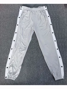 Detailweergave van een grijze sportbroek met drukknopen aan de zijkant en witte strepen.