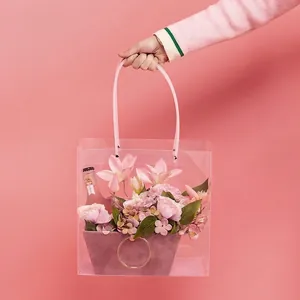 Borsa regalo trasparente per fiori con lunghi manici rosa e composizione floreale.