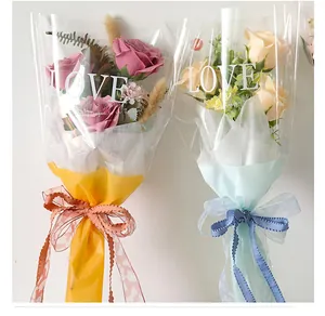Detailed view of transparent bouquet wrapping bags featuring white 'LOVE' text and elegant ribbons