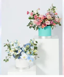 Elegantes cajas de regalo redondas con arreglos florales sobre pedestales blancos