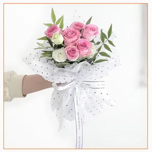 Primo piano di elegante carta velina a pois che avvolge un bouquet di rose rosa fresche.