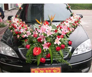 Wedding car flower arrangement with lilies and roses on a black vehicle hood setup.
