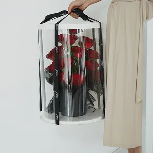 Hand-held view of a large transparent cylindrical PVC flower gift box with black ribbons
