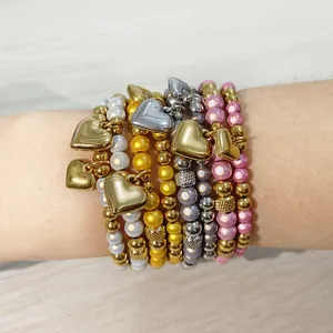 Dettaglio di braccialetti impilati con perline colorate in acciaio inox e ciondoli a cuore