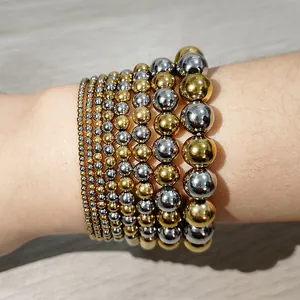 Close-up of stacked gold and silver stainless steel bead elastic bracelets on wrist