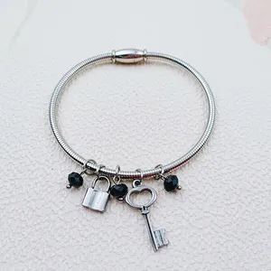 Close-up detail of a silver stainless steel charm bracelet with lock and key pendants