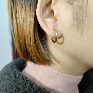 Détail macro montrant une boucle d'oreille créole minimaliste en acier titane doré