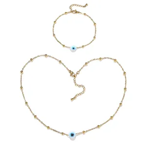 Detail view of gold bead chain necklace and bracelet set with blue evil eye charms.