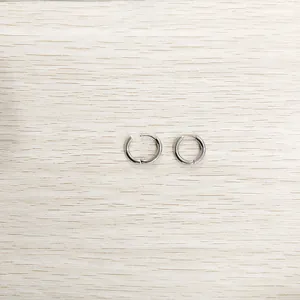 Vue détaillée de petites boucles d'oreilles en acier titane argenté sur fond de bois.