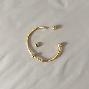 Detail shot of a golden titanium steel open bangle with an unscrewed ball end feature.