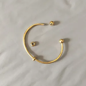 Close-up detail of gold titanium steel bangle showing the detachable screw ball mechanism
