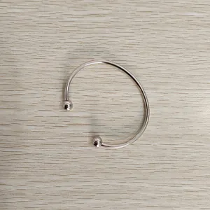 Minimalist stainless steel open bangle with unscrewable ball ends on wood background