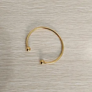Elegant gold stainless steel ball end open cuff bracelet displayed on a light wood background