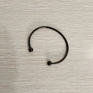 Top view of a black stainless steel open cuff bracelet with ball ends on wood background