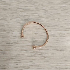 Macro view of a polished rose gold stainless steel open bangle with decorative ball ends.