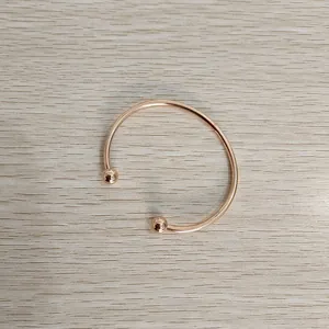 Detail of rose gold stainless steel open bangle with ball head ends on wood background