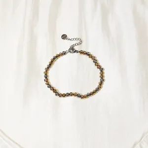 Nahaufnahme eines dreifarbigen Edelstahl-Armbands mit facettierten Perlen auf weißem Stoff