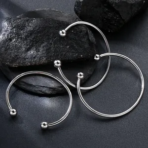 Minimalist stainless steel open bangle with screwable ball ends on black stone texture.