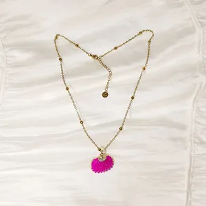 Primer plano de un colgante de concha rosa vibrante en un collar de cadena dorada.