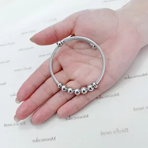 Close-up of a silver stainless steel wire bracelet with polished round beads held in hand.